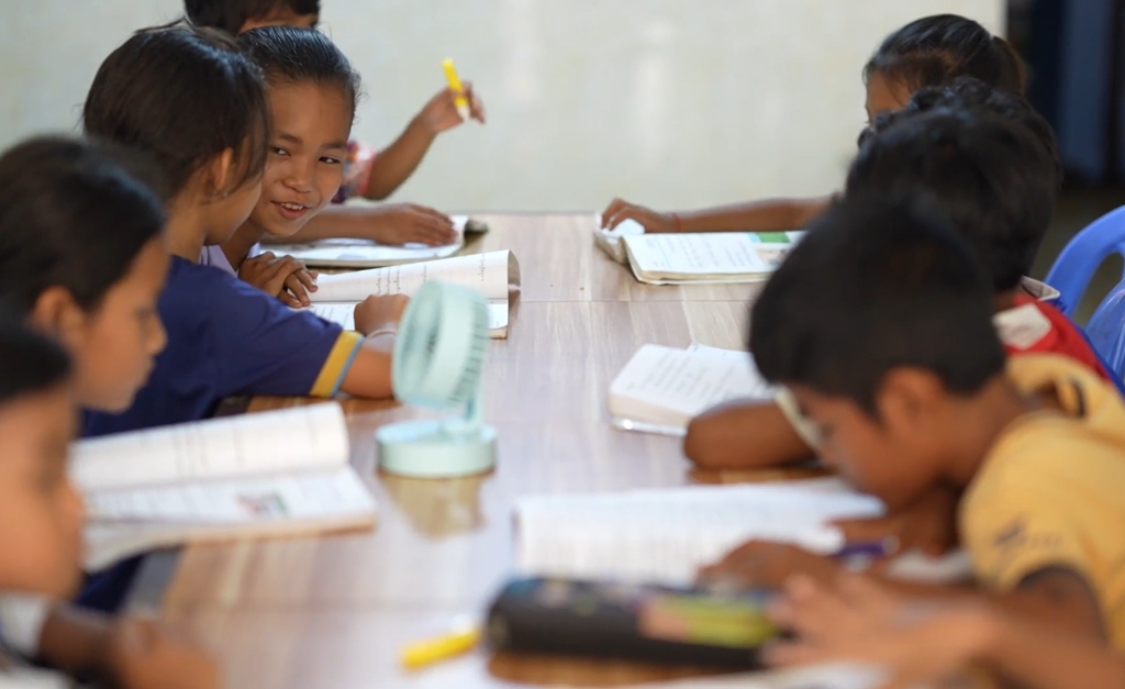 Kids sit at table smiling and learning